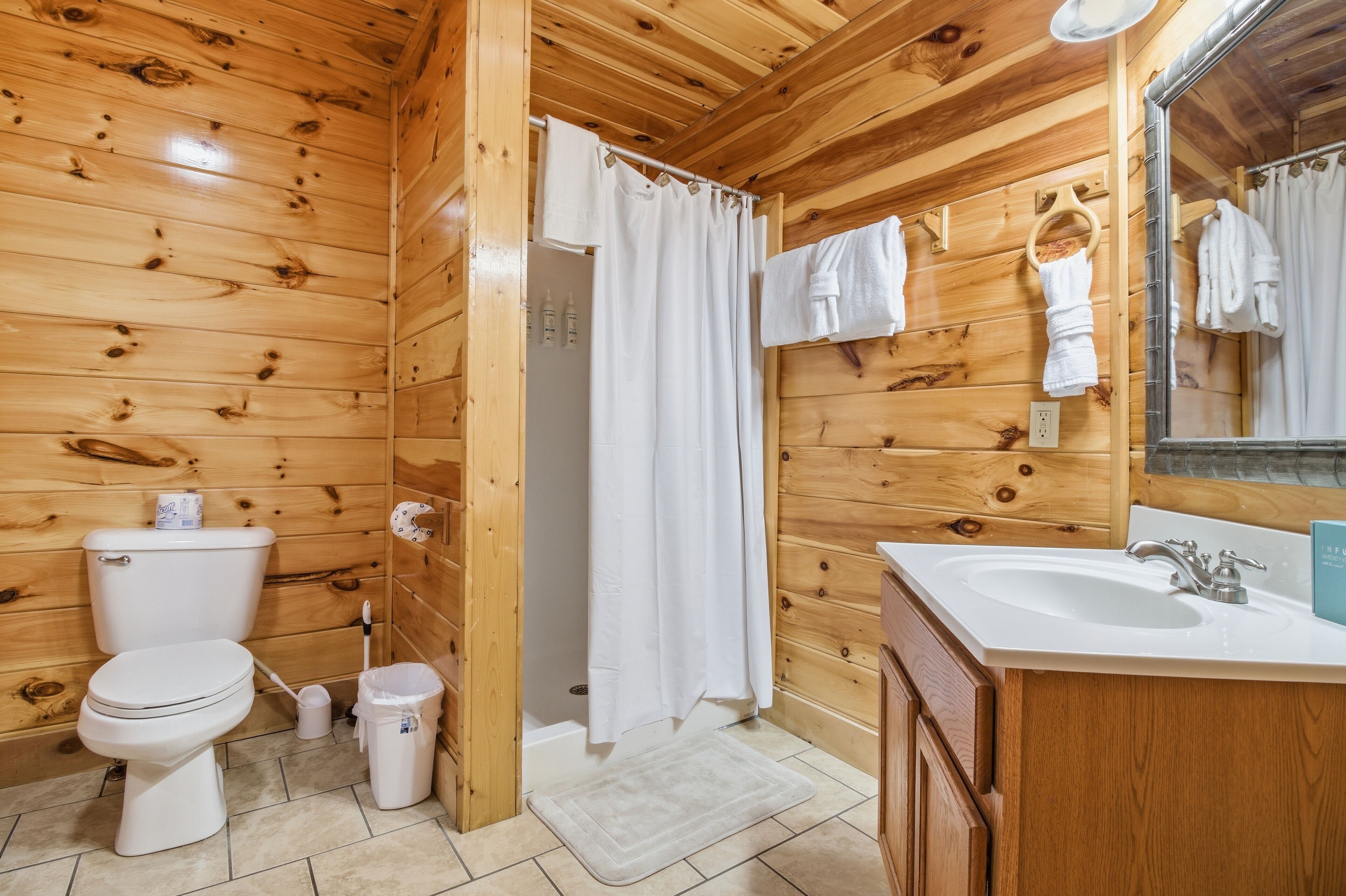 Baño de cabaña de madera con inodoro, lavamanos y cortina de ducha.