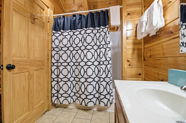 A wooden cabin bathroom with a shower curtain, a bathtub, and a towel rack. - Just For Fun (Sevierville)