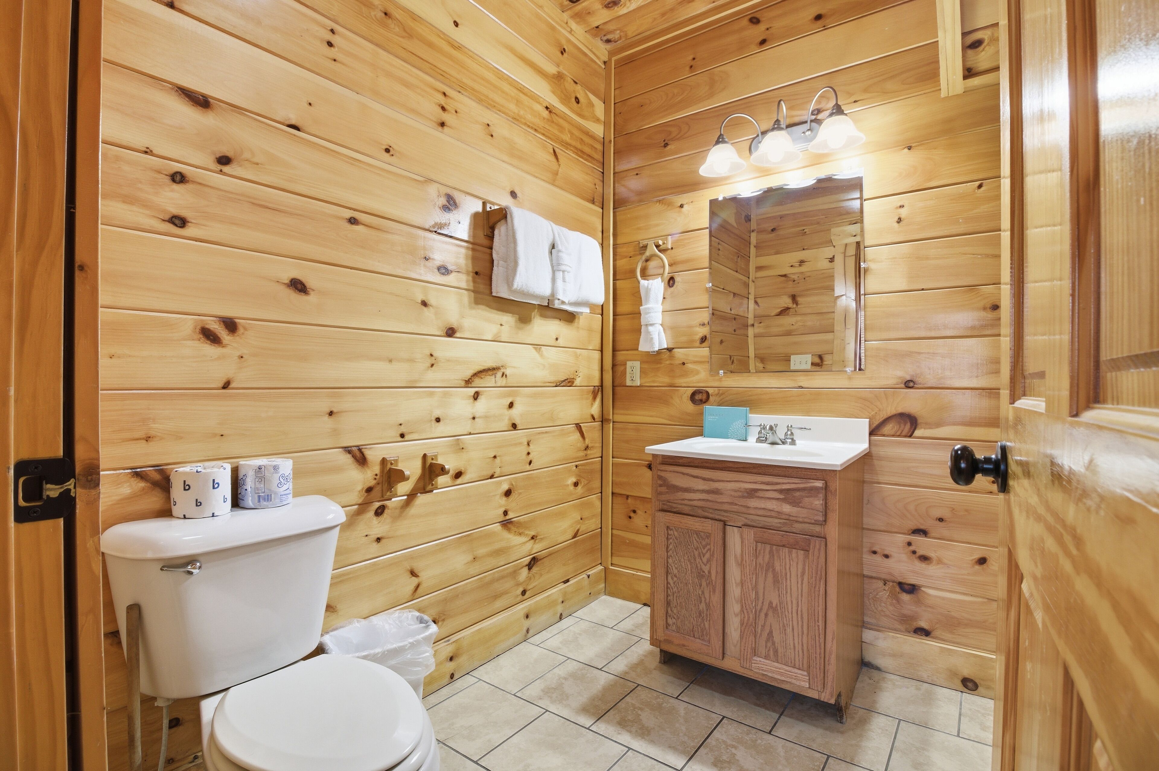 A wooden-paneled bathroom with a toilet, sink, and mirror.