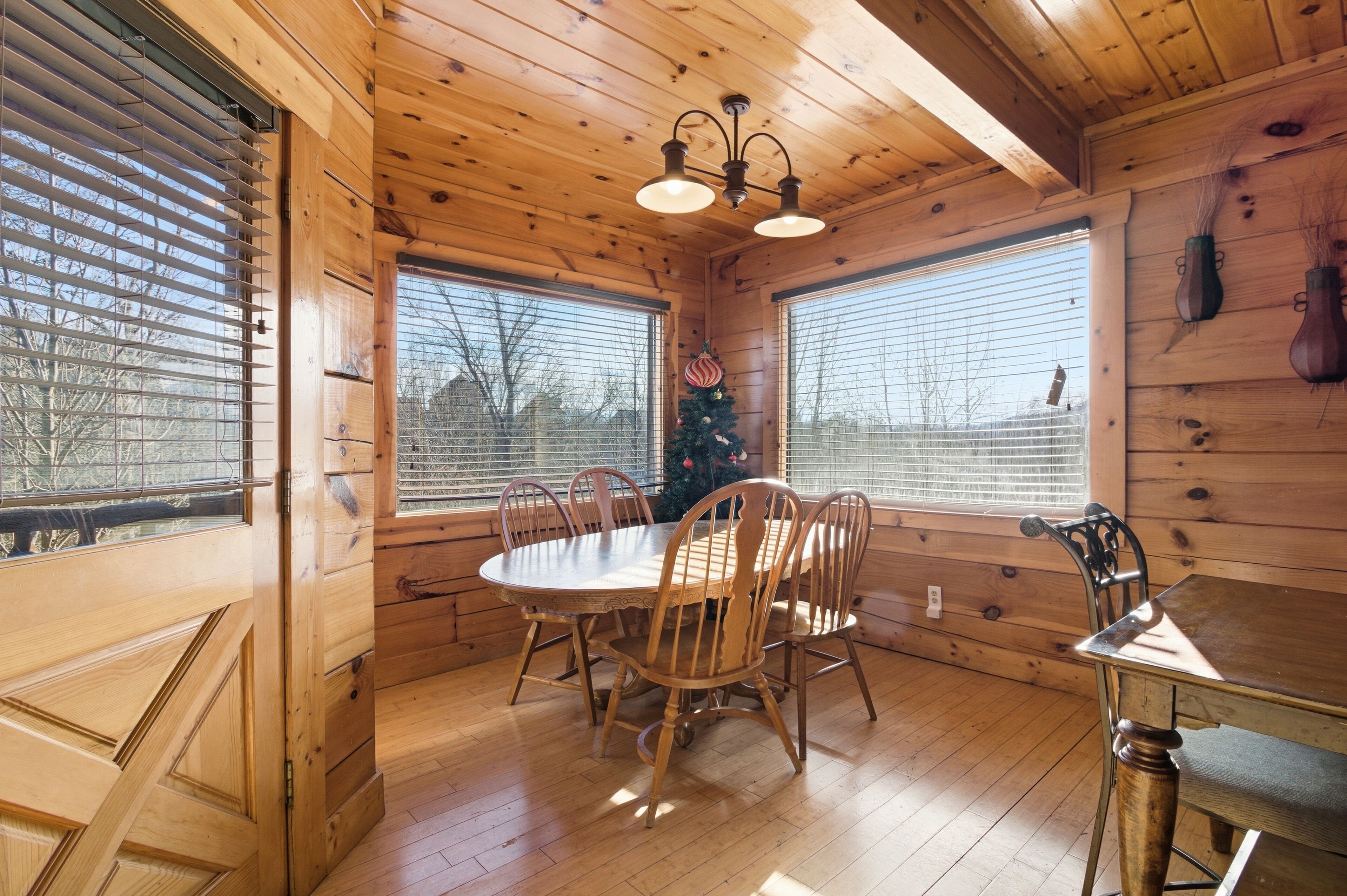 A wooden cabin interior with a dining table, chairs, and a Christmas tree.