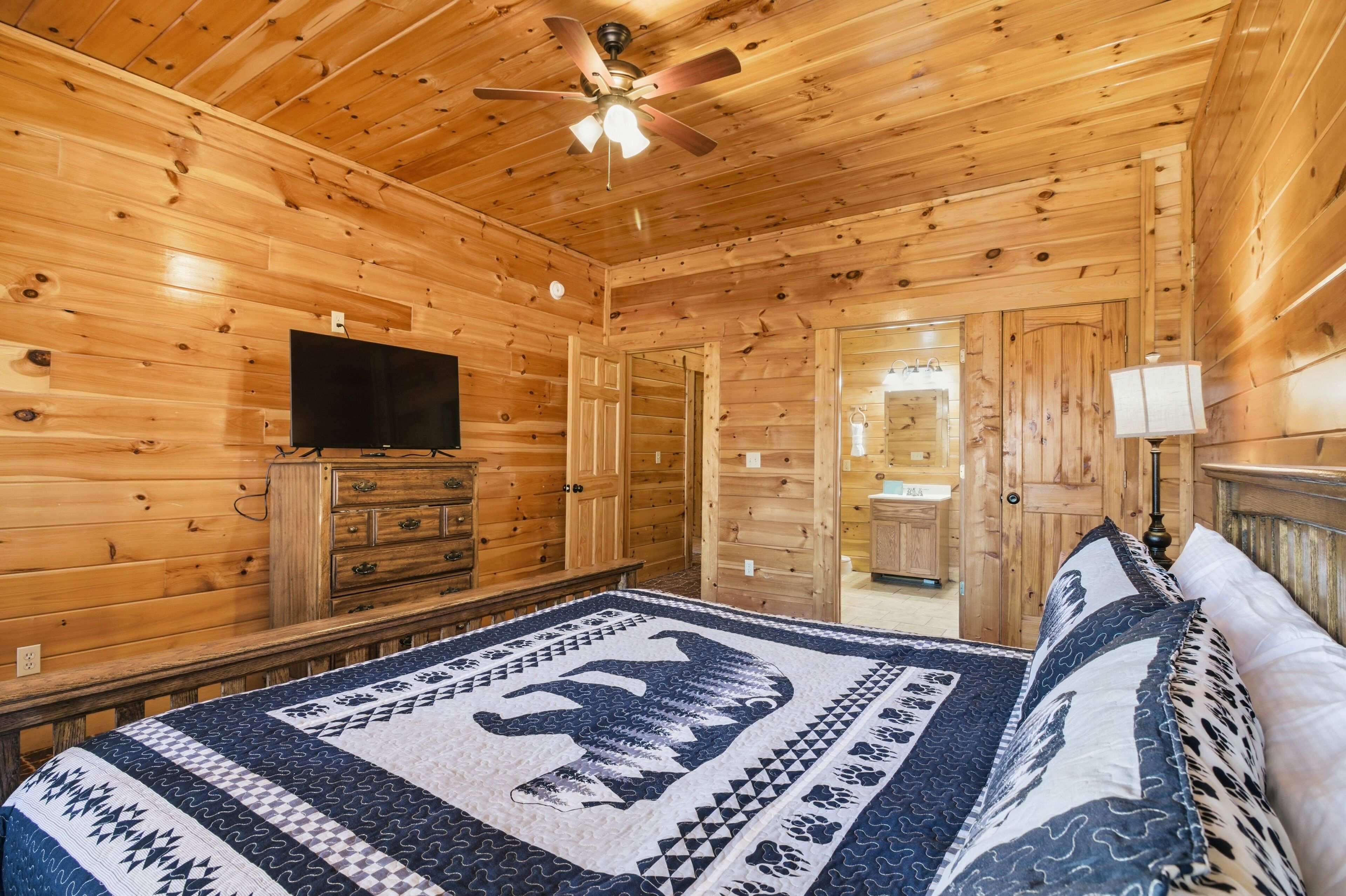 Une chambre dans une cabane en bois, avec un lit, une commode, une télévision et un ventilateur de plafond.