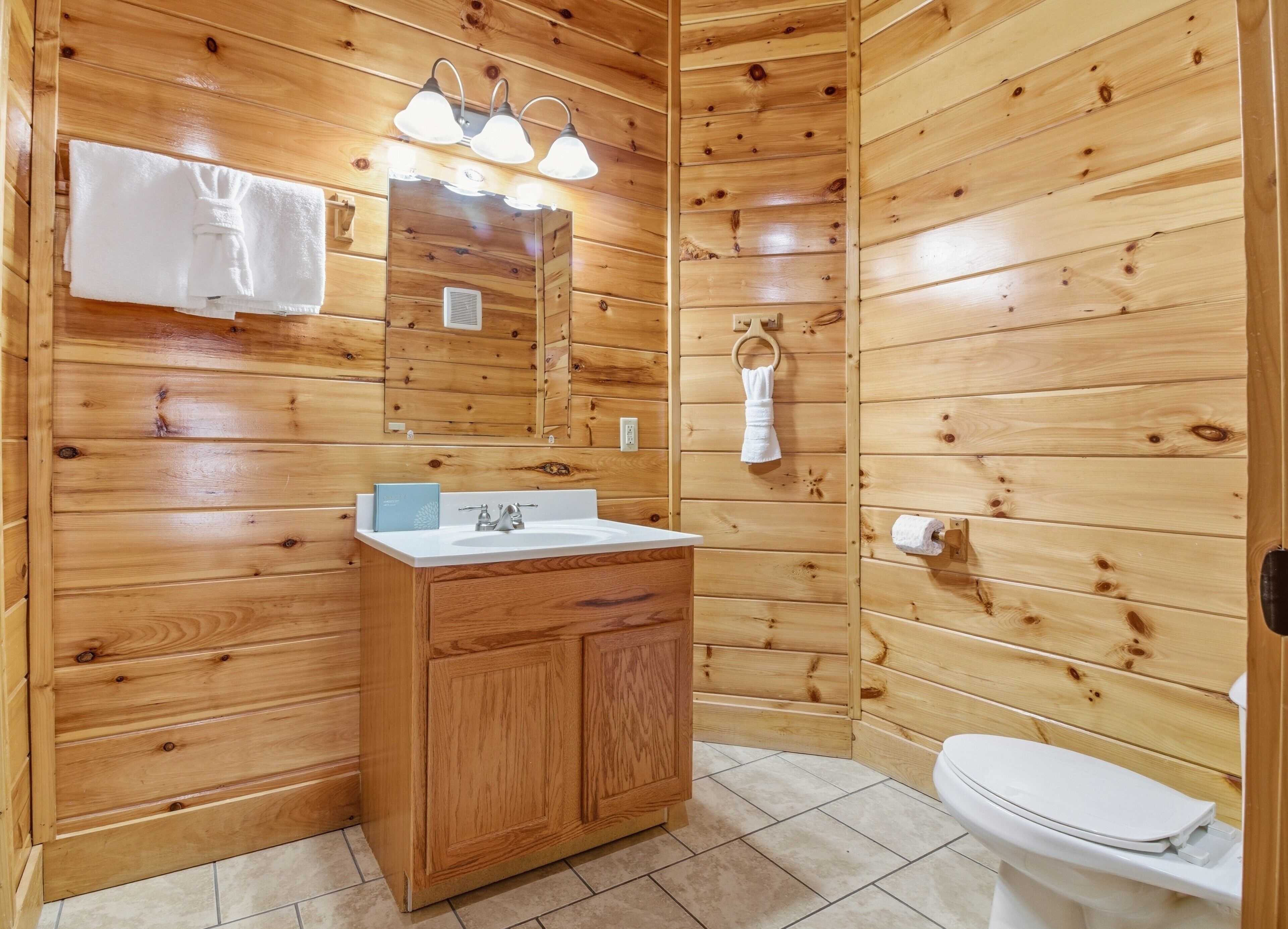 A wooden-paneled bathroom with a sink, mirror, and toilet.
