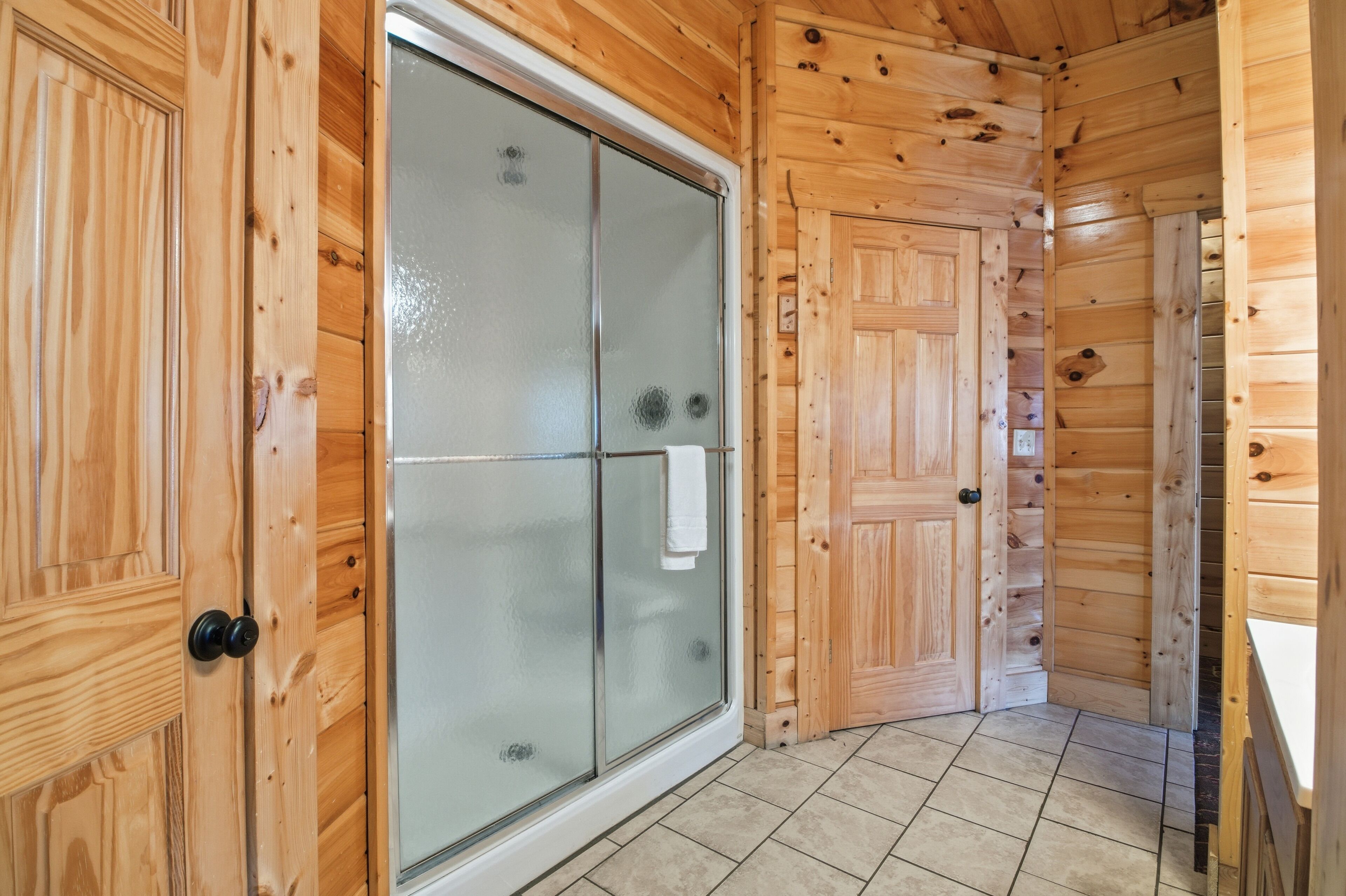 A wooden cabin interior with a glass shower door, wooden walls, and a tiled floor.