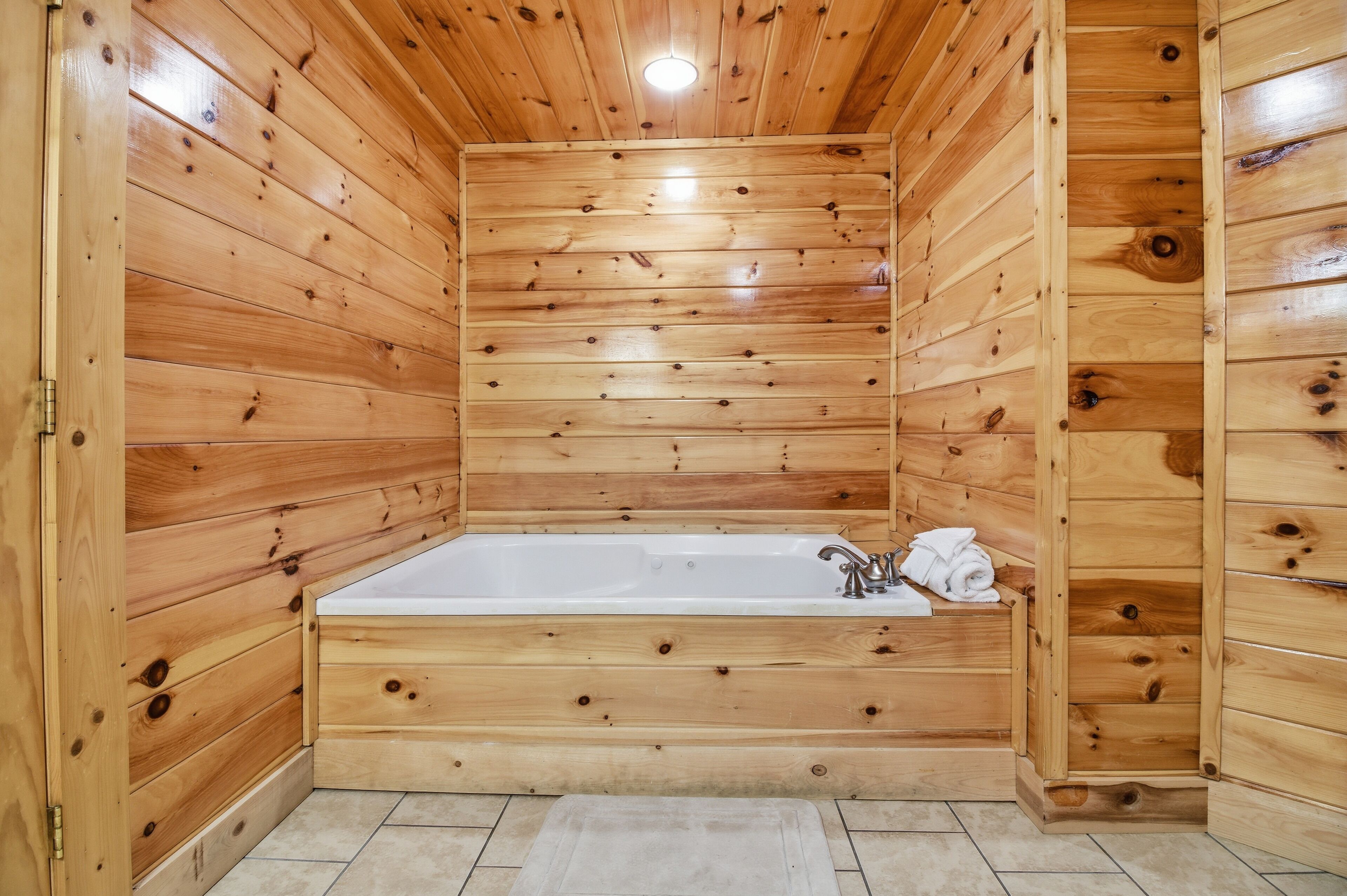 A wooden cabin with a large bathtub, wooden walls, and a tiled floor.
