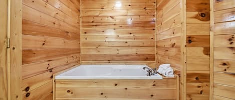 A wooden cabin with a large bathtub, wooden walls, and a tiled floor.