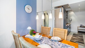 A dining area with a table set for two, a clock on the wall, and a kitchen in the background. - Baden-Chalet – Charming Apartment with Views over the Rhine Valley (Bühl)