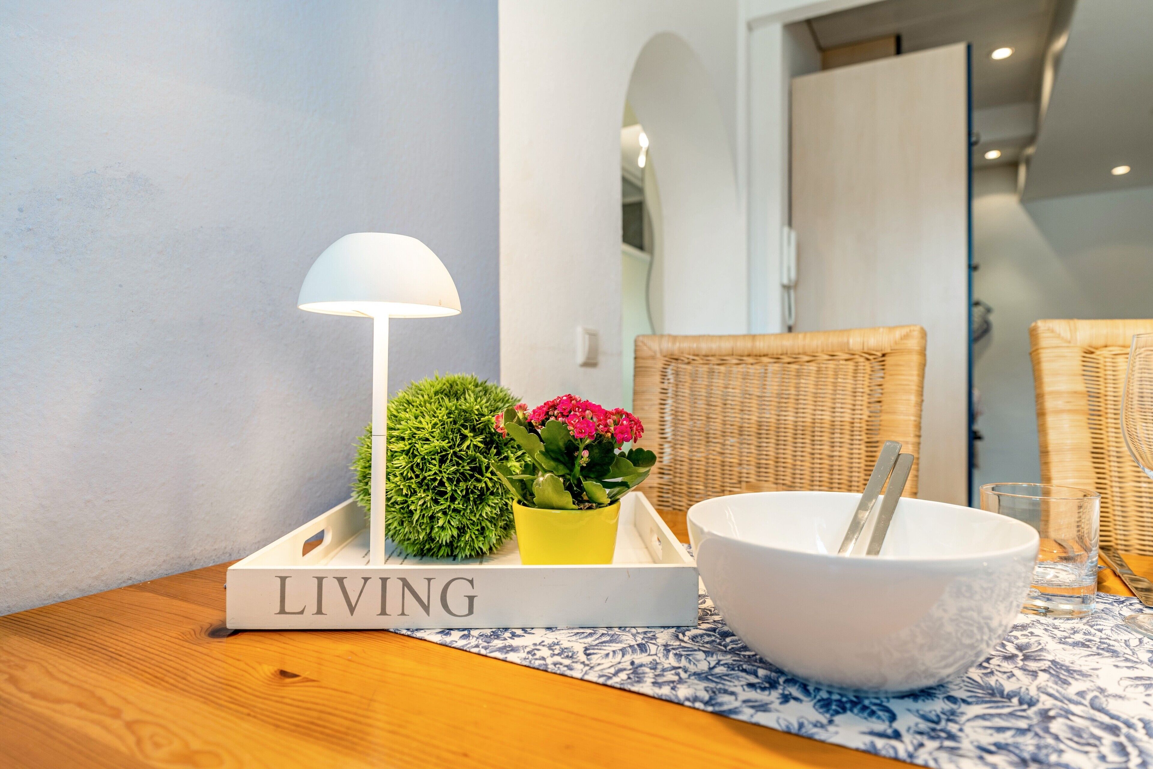 Ett rum med ett vitt bord, en vit skål med en sked, en krukväxt, en lampa och en bok med titeln ”LIVING”.