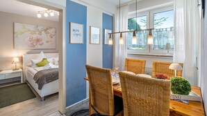 A modern hotel room with a bed, a dining area with wicker chairs, and a view of the outdoors through large windows. - Baden-Chalet – Charming Apartment with Views over the Rhine Valley (Bühl)