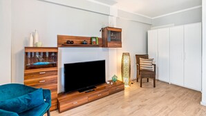 A modern living room with a flat-screen TV, wooden furniture, a blue chair, and a white wardrobe. - Baden-Chalet – Charming Apartment with Views over the Rhine Valley (Bühl)