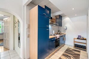 A modern kitchen with a blue and wooden cabinet design, a built-in oven, and a small wooden shelf with kitchen items. - Baden-Chalet – Charming Apartment with Views over the Rhine Valley (Bühl)