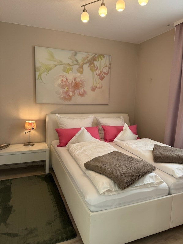 Un lit bien fait, avec une literie blanche et rose, une lampe de chevet et une œuvre d’art florale accrochée au mur.
