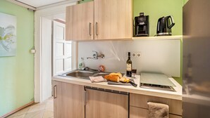 Una cocina con armarios de madera, un lavamanos, una cafetera, una botella de vino y una tabla de cortar con pan.