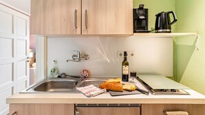 Una cocina con armarios de madera, un lavamanos de acero inoxidable, una cafetera, una botella de vino y una hogaza de pan.