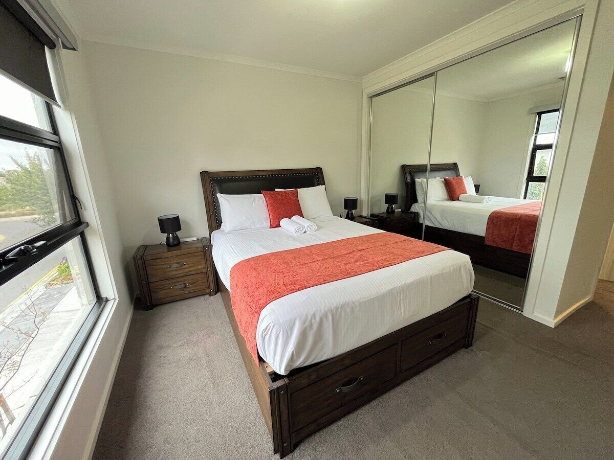 Une chambre à coucher avec un grand lit, une table de chevet en bois, un miroir et une fenêtre.