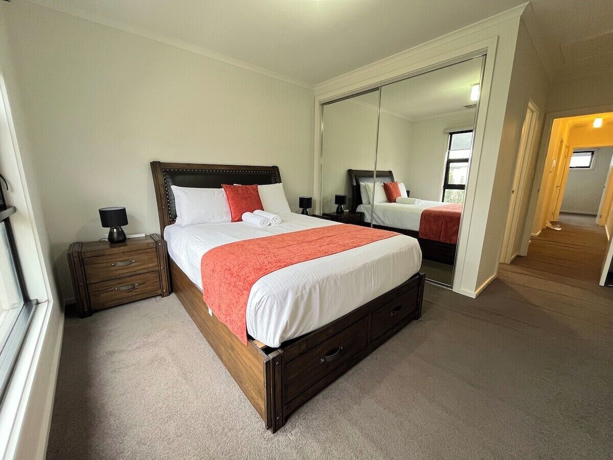 A neatly arranged bedroom with a large bed, a nightstand, a mirror, and a carpeted floor.