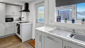 Una cuina moderna amb armaris blancs, forn integrat i finestra amb vista a l'exterior.