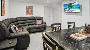 Un saló modern amb un sofà de pell negra, una taula de dinar amb cadires, un televisió de pantalla plana i obres d'art a les parets.