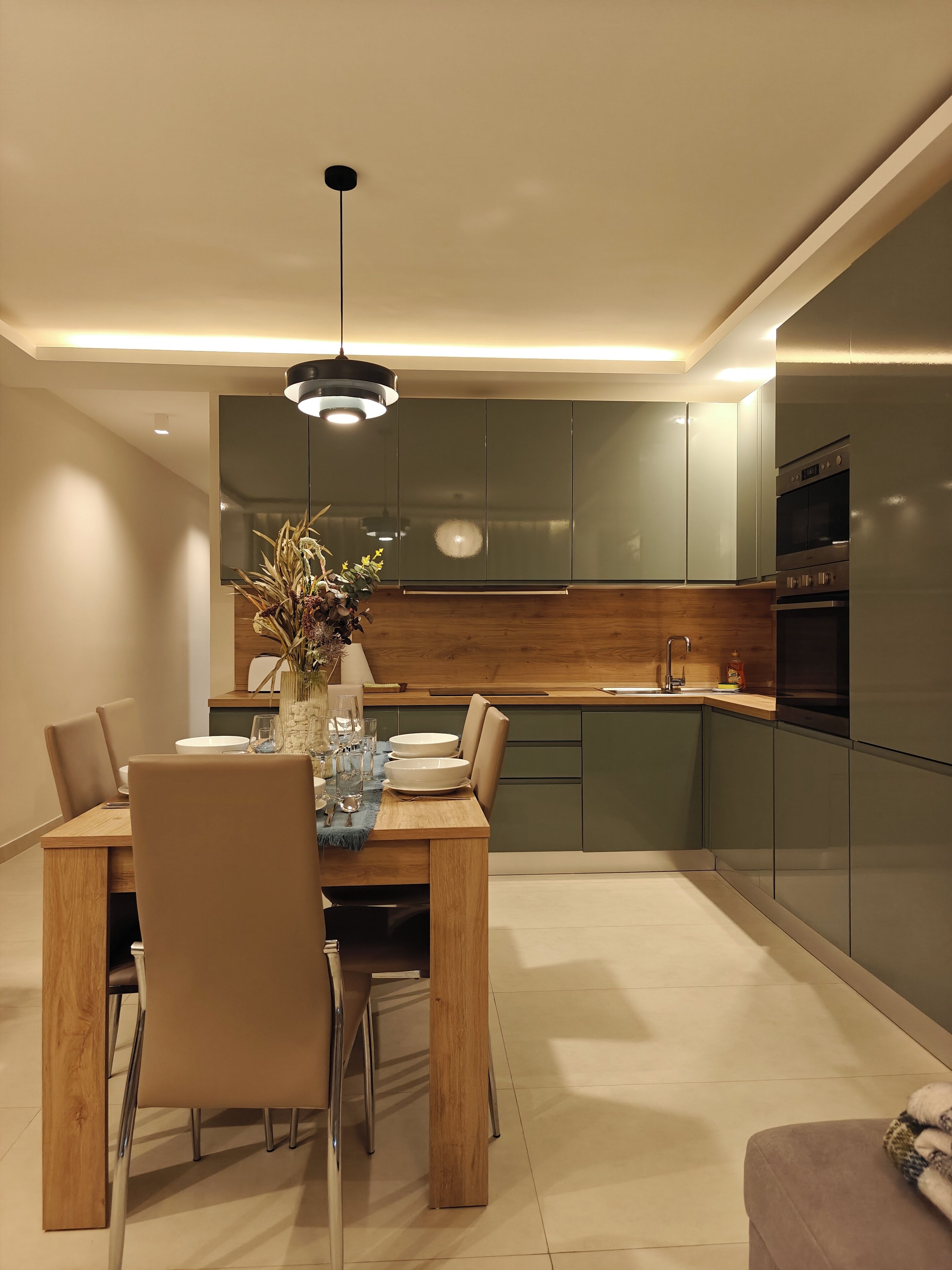 Une cuisine moderne avec des meubles de couleur sombre, une table à manger en bois et un luminaire suspendu.