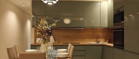 Une cuisine moderne avec des meubles de couleur sombre, une table à manger en bois et un luminaire suspendu.