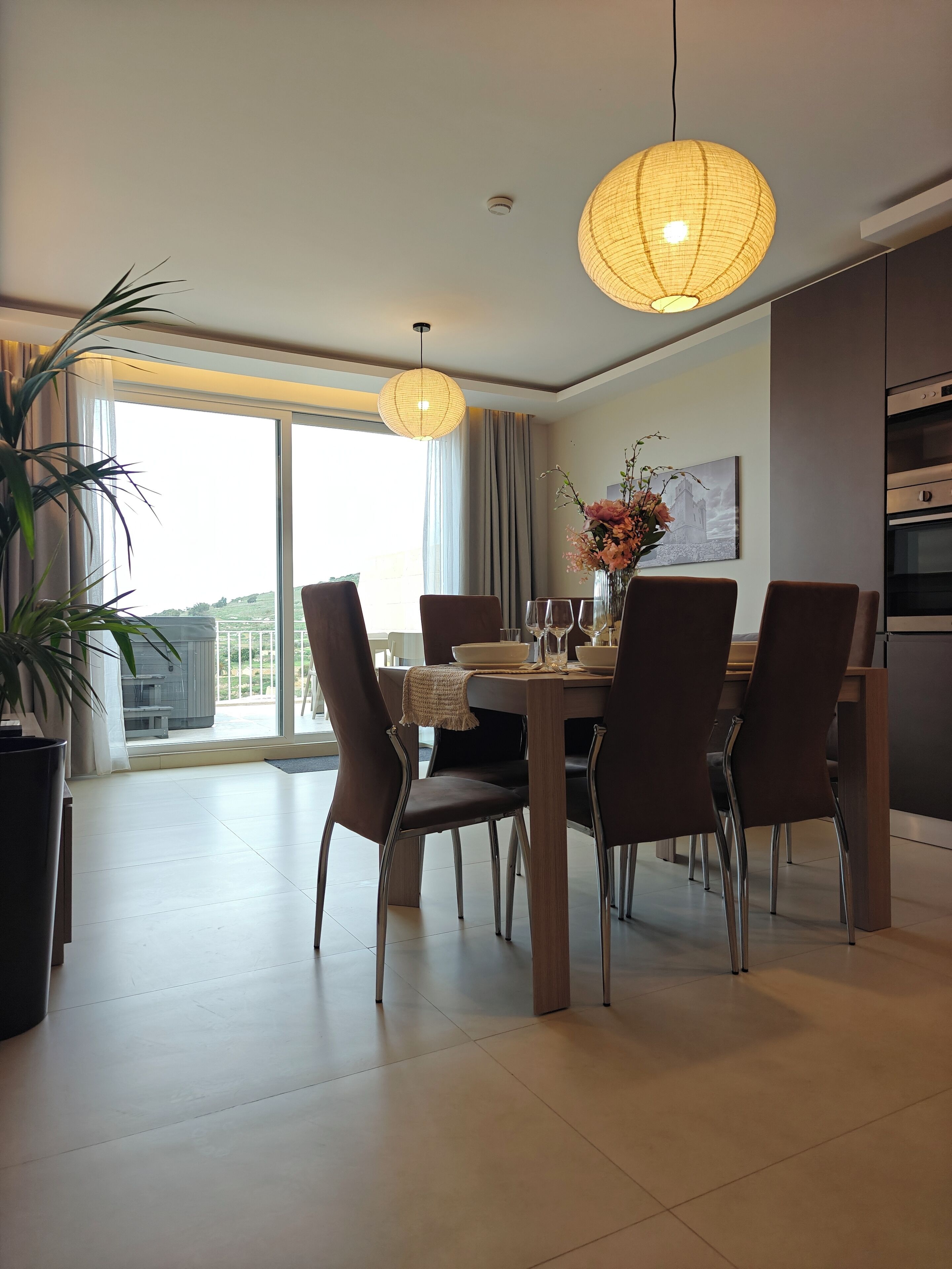 A modern dining area with a large table, chairs, and pendant lighting.