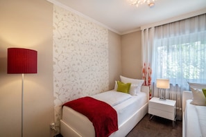 Un dormitorio con una cama, una mesita de noche, una lámpara y una ventana con cortinas.