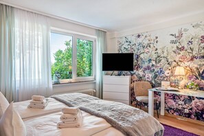 Une chambre d’hôtel avec un lit, un bureau, une chaise, une télévision et une fenêtre avec des rideaux.