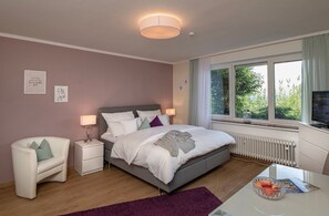 Ein Schlafzimmer mit einem Bett, Nachttischen, einem Sessel, einem Fenster mit Blick und einem Fernseher.