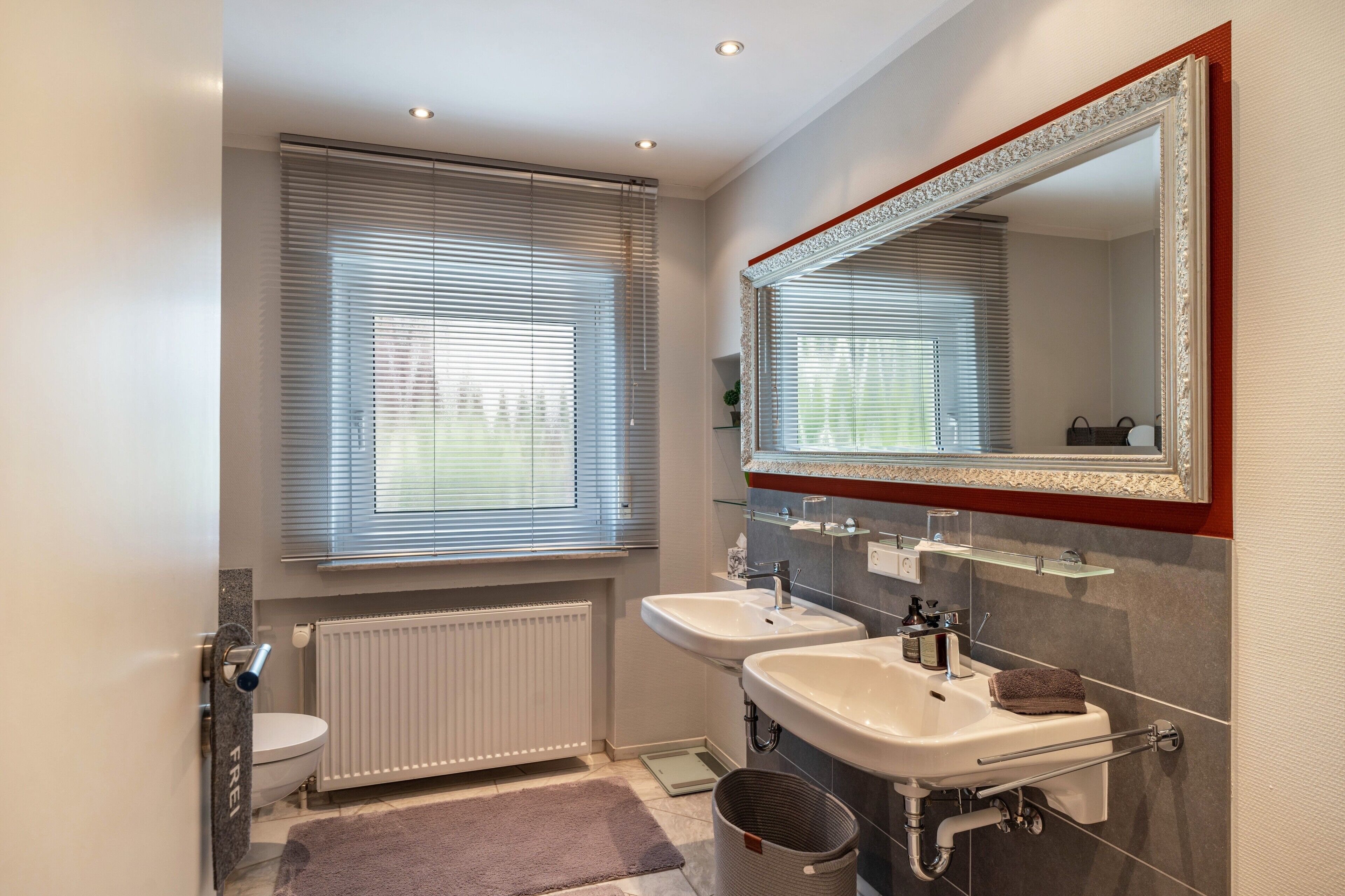 Ein modernes Badezimmer mit zwei Waschbecken, einer Toilette, einem Heizkörper und einem großen Spiegel.
