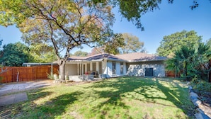 A house with a covered porch, a fenced yard, and a large tree providing shade.
