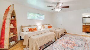 A bedroom with two beds, a ceiling fan, a window with blinds, and a patterned rug.