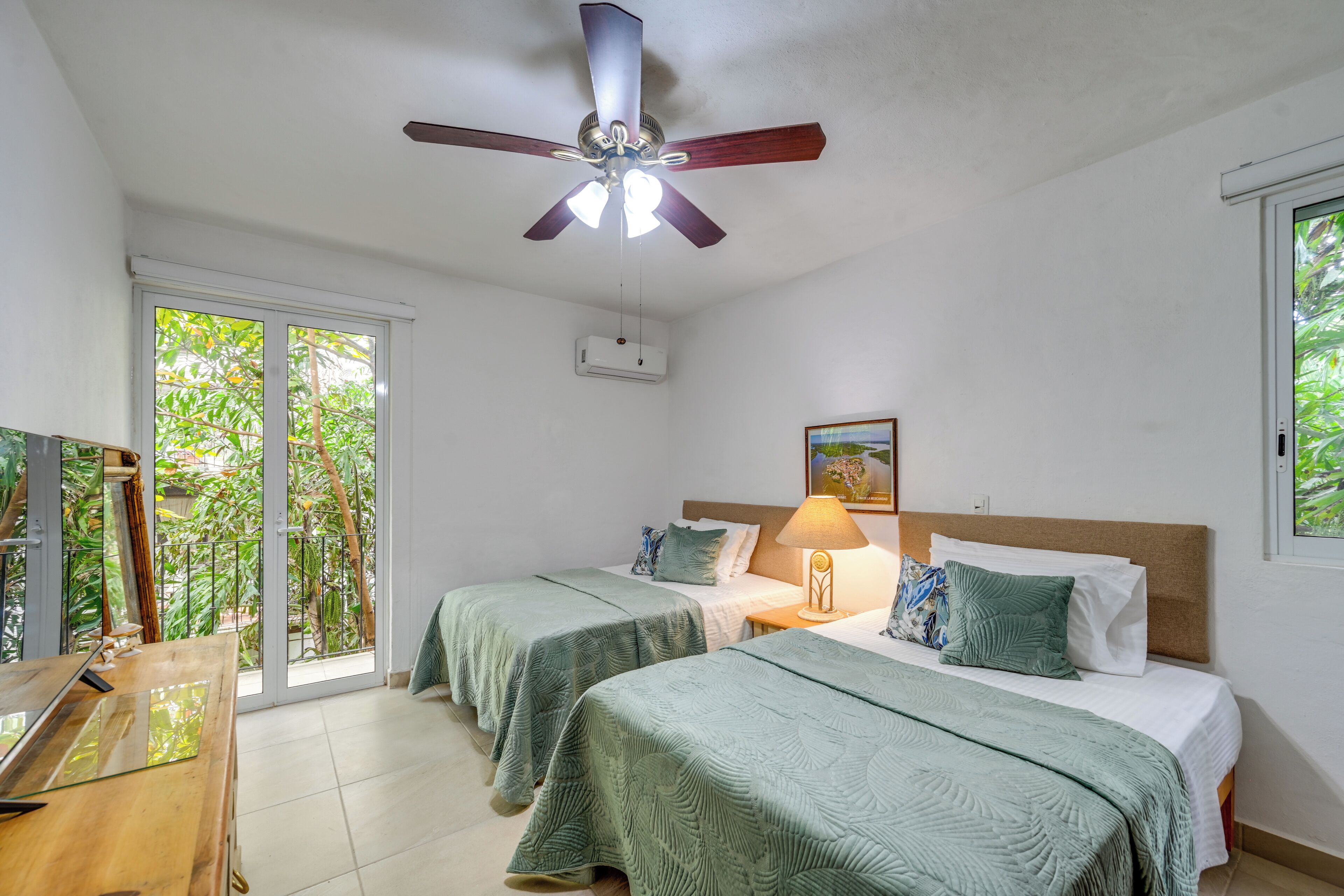 Camera d'albergo con due letti, una ventola a soffitto, una finestra e vista su del verde all'esterno.