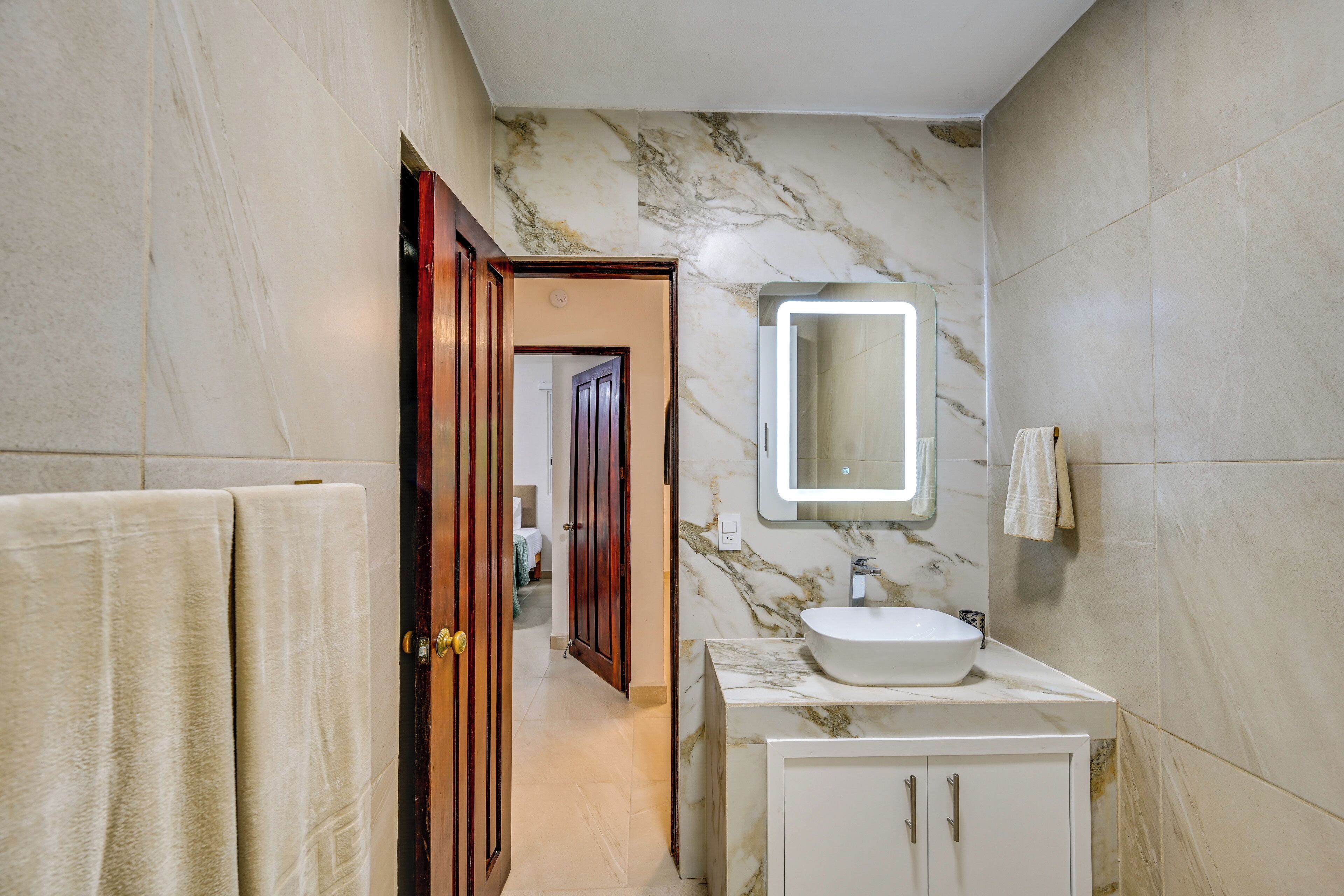 A bathroom with a marble wall, a sink, and a mirror.