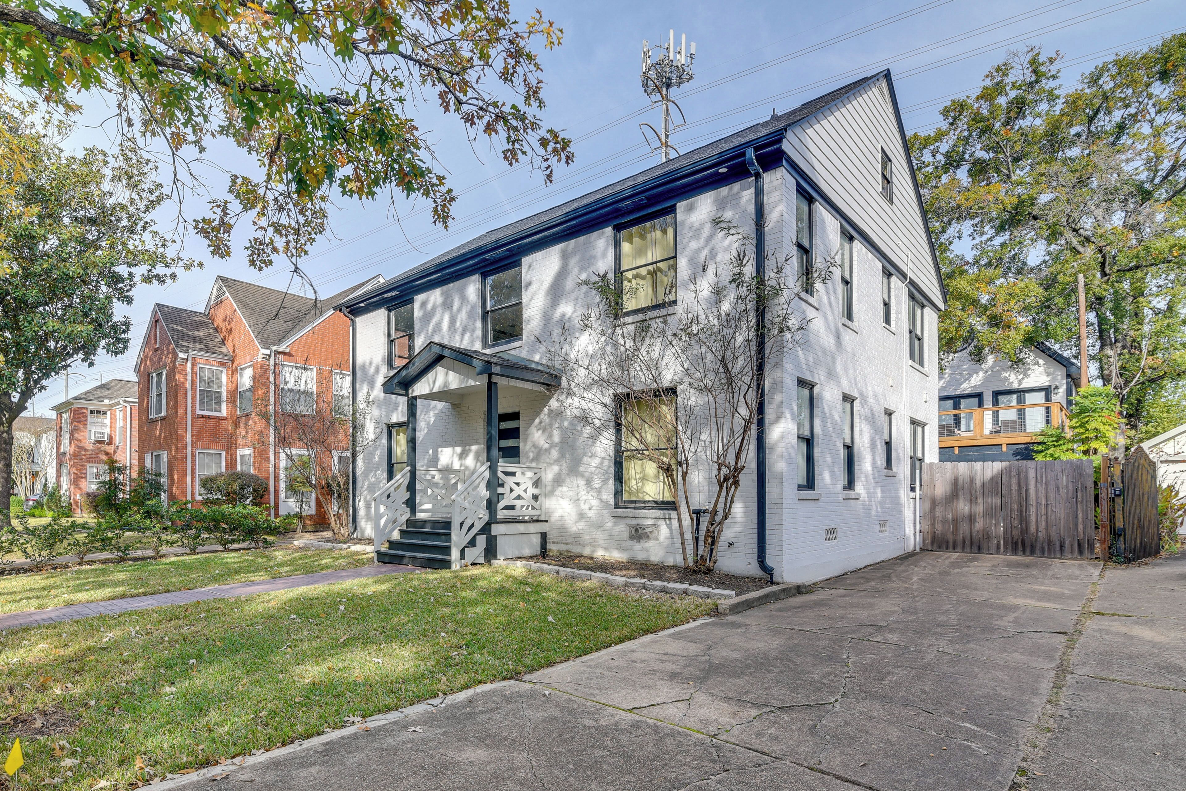 A two-story residential building with a front porch, a small front yard, and a wooden fence.
