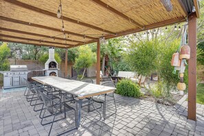 An outdoor patio with a brick floor, a wooden pergola, a grill, a table with chairs, and a hanging bell. - Luxurious Outdoor Oasis! Spacious Mesa Retreat (Mesa)