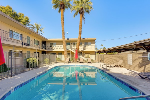A swimming pool with lounge chairs and palm trees, surrounded by a building with balconies and a fence. - Summer-ready Old Town Condo w/ Pool & Patio Access (Scottsdale)