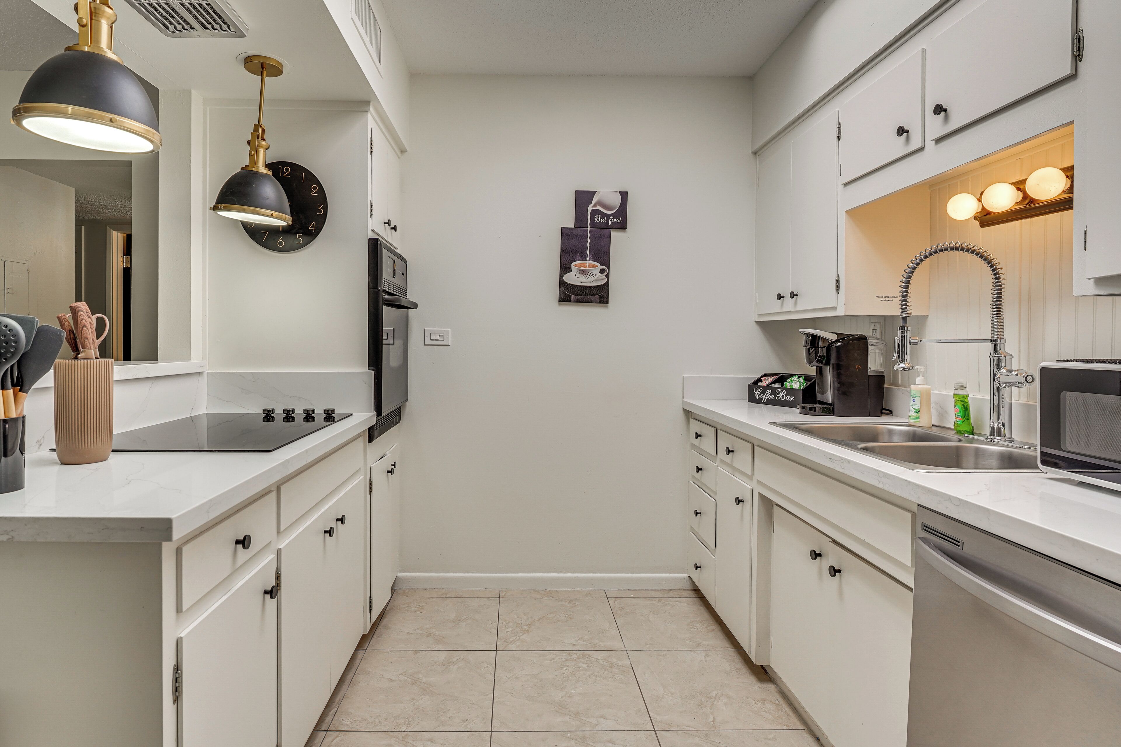 Una cocina moderna con armarios blancos, una estufa negra y un lavamanos. Hay un reloj en la pared y una cafetera sobre la encimera.