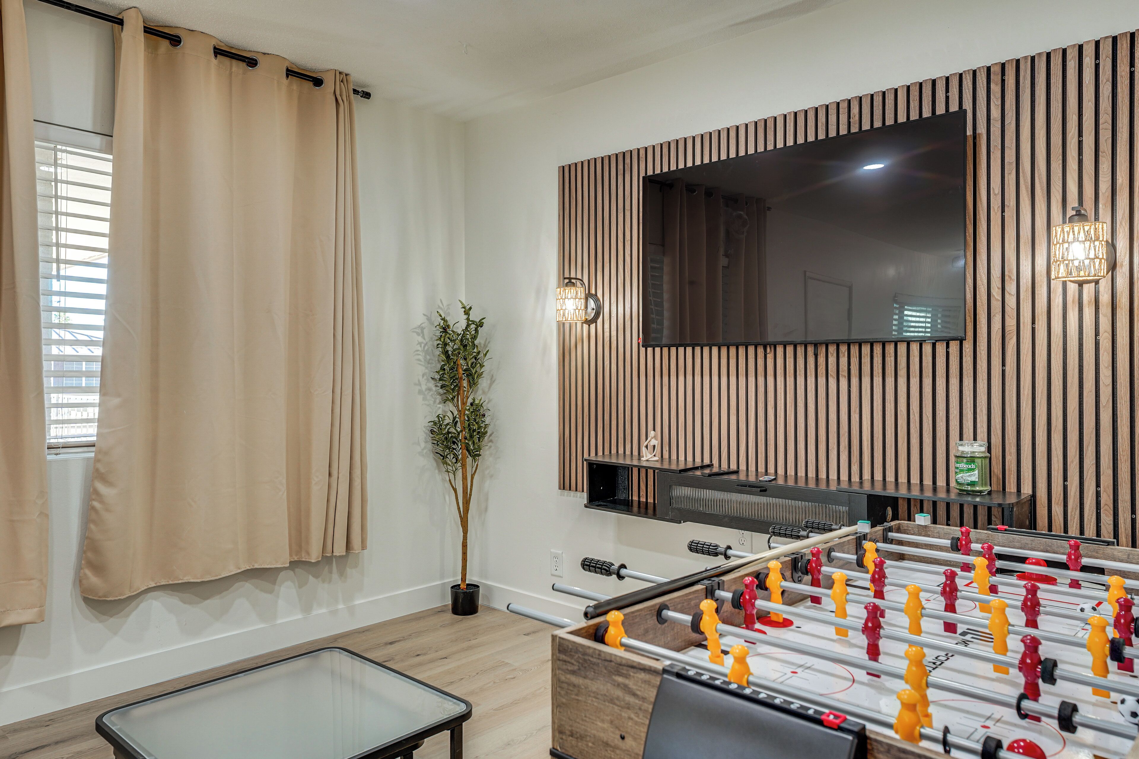 Ein Zimmer mit Kicker, einem an einer Holzvertäfelung montierten Fernseher, einem Blumentopf und einem kleinen Tisch.