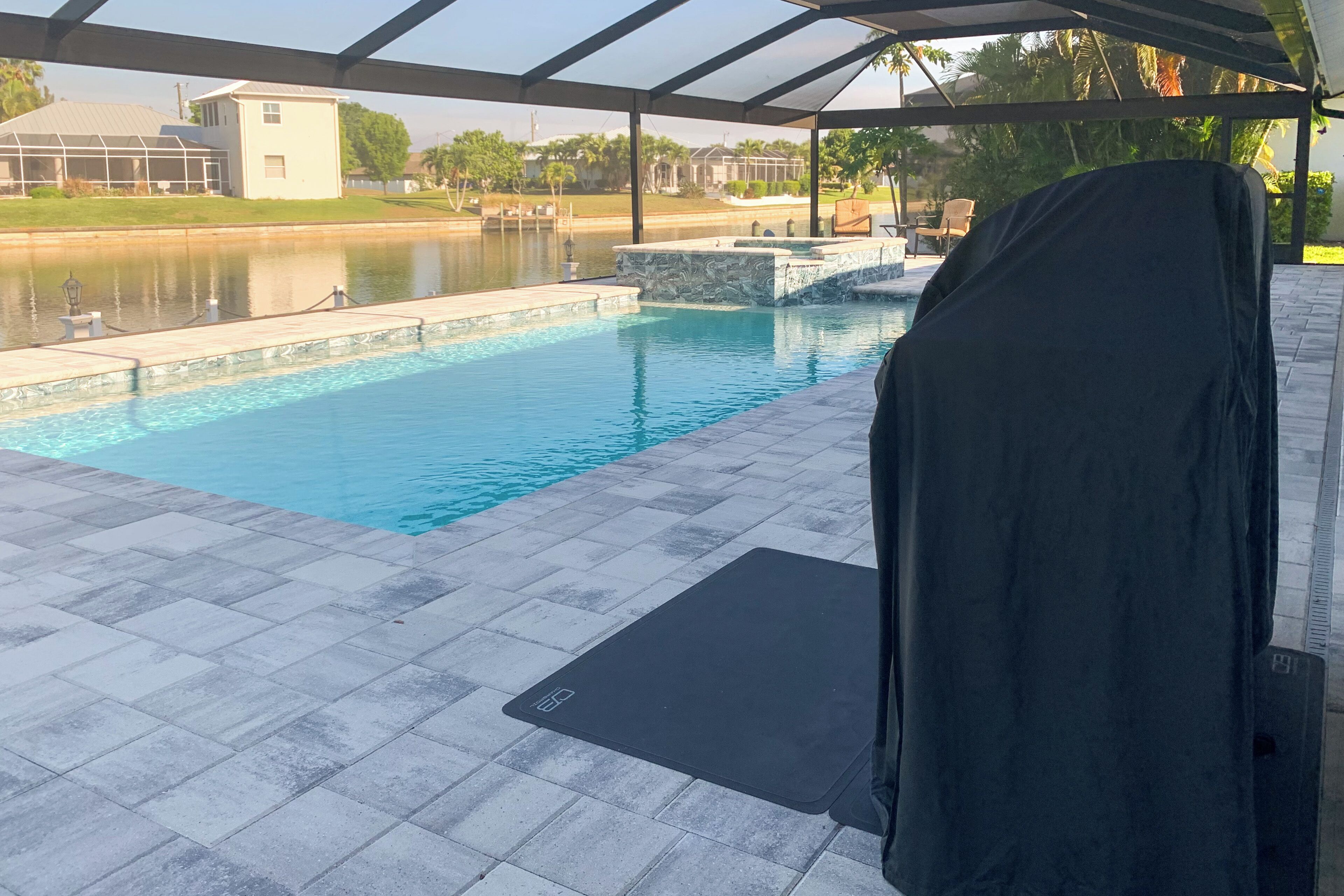 Ein Pool mit überdachter Terrasse, Blick auf ein Haus gegenüber dem Wasser und einem überdachten Sitzbereich.