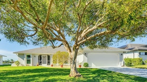 A single-story house with a large tree in the front yard, a garage, and a well-maintained lawn. - Waterfront Cape Coral Gem w/ Lanai, new Pool & Spa (Cape Coral)