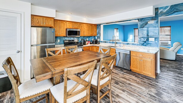A modern kitchen with wooden cabinets, stainless steel appliances, a marble backsplash, and a dining area with a wooden table and chairs. - Hot Tub & Sauna! Atlantic City Getaway By Beach (Atlantic City)
