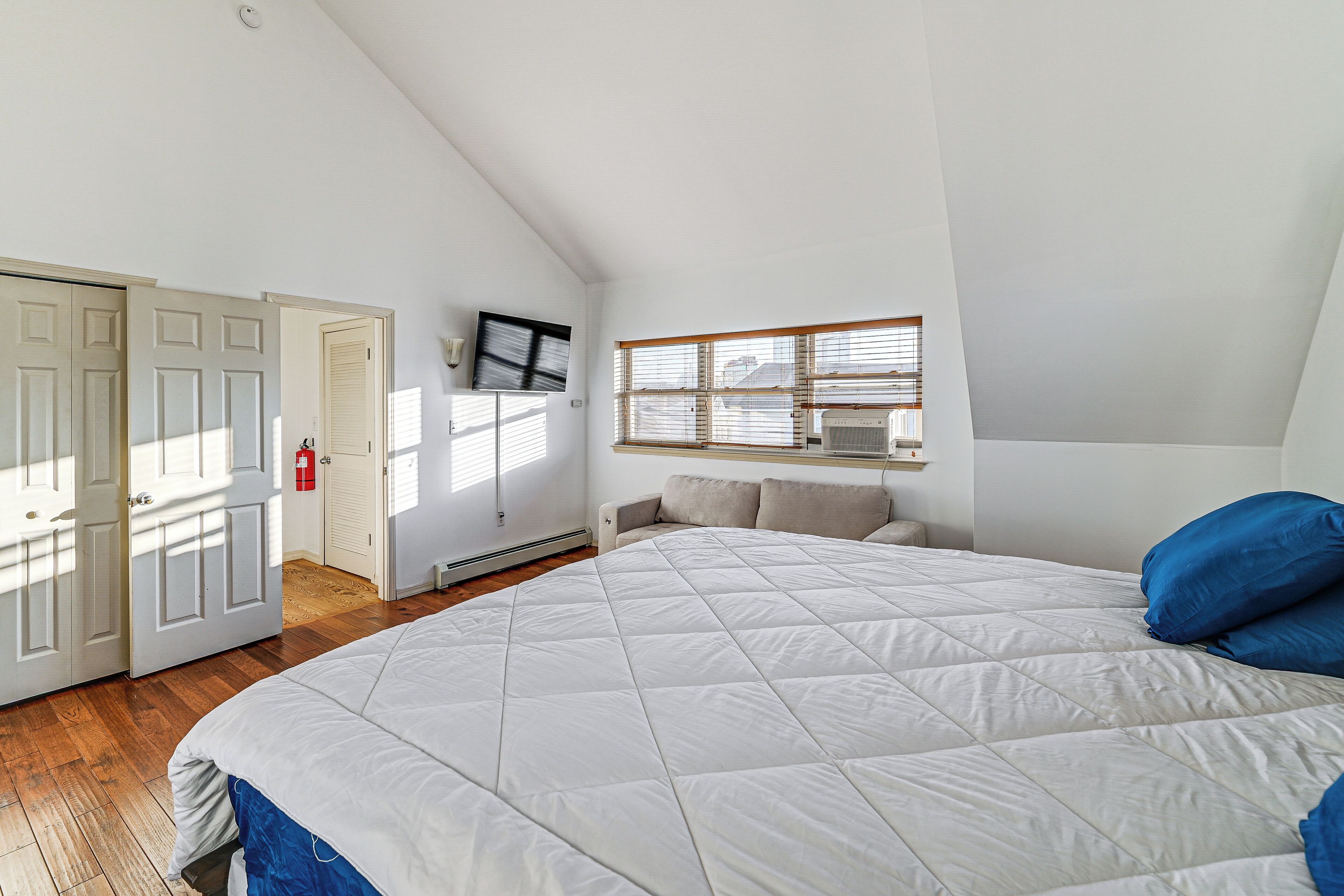 A bedroom with a large bed, a window with blinds, a ceiling fan, and a door.