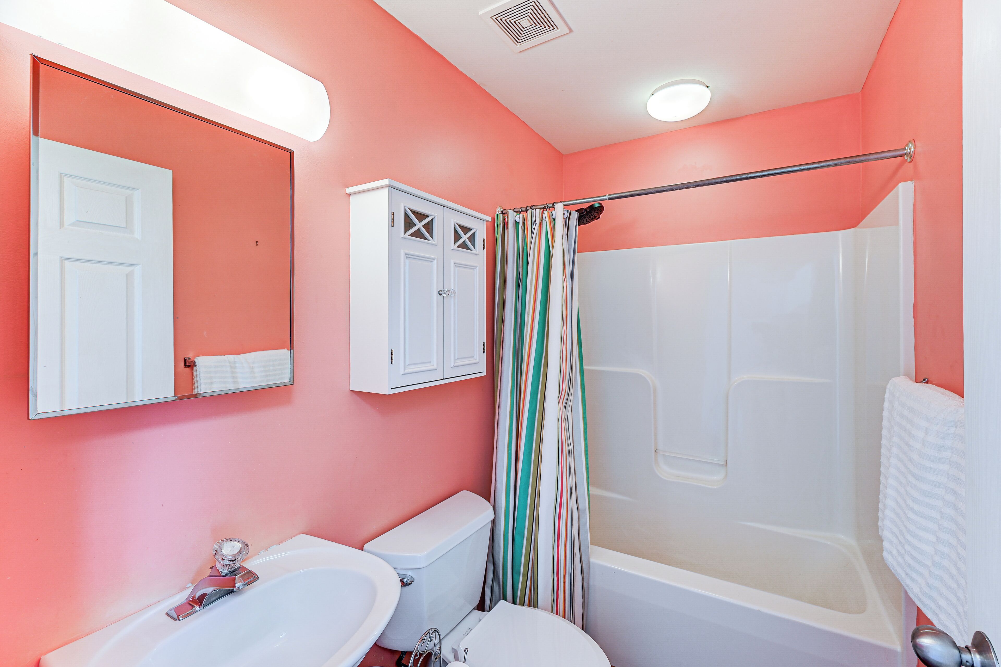 A bathroom with a white sink, toilet, and bathtub, a striped shower curtain, and a mirror above the sink.