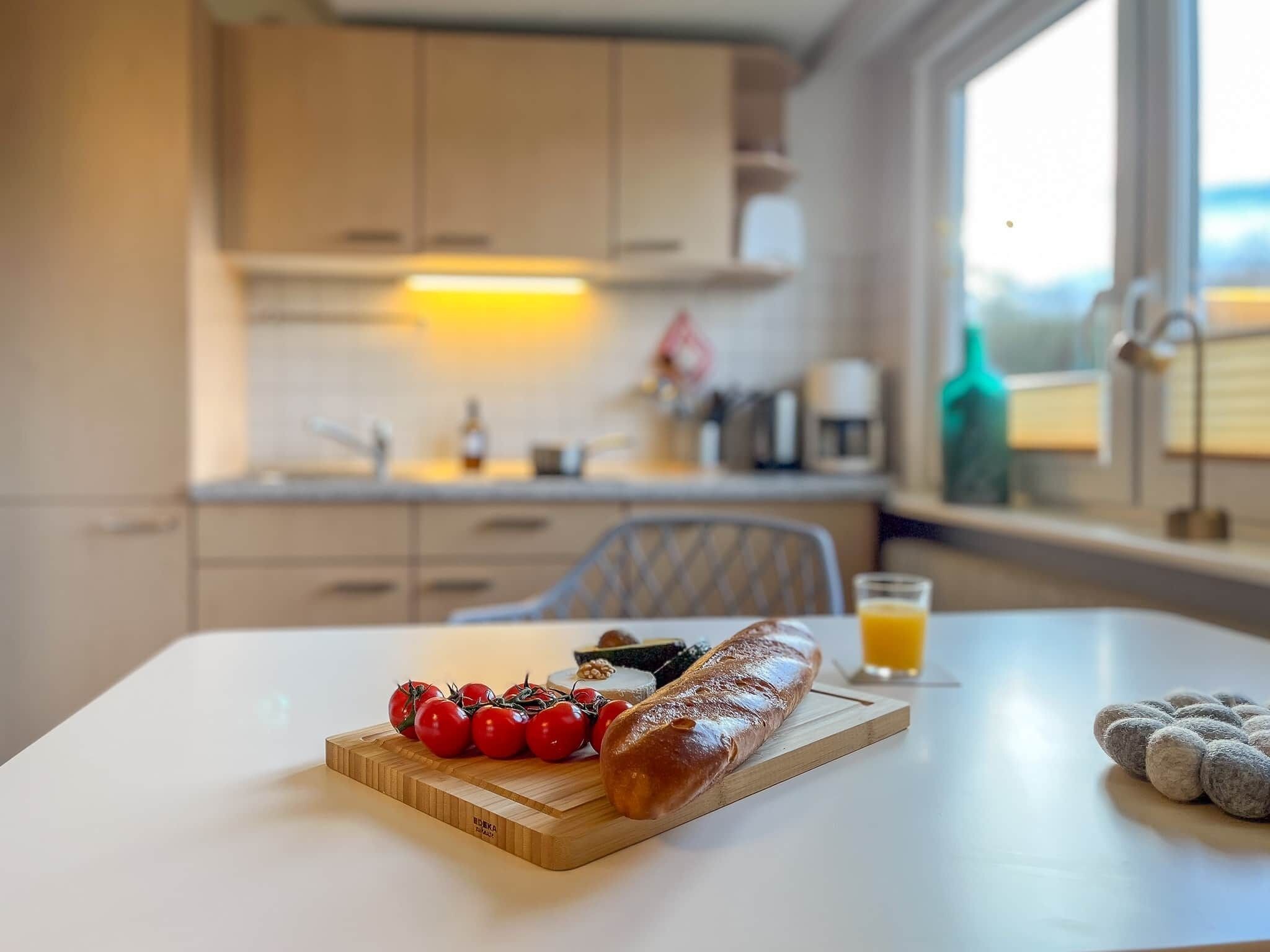 A kitchen with a wooden table, a loaf of bread, cherry tomatoes, and a glass of orange juice.