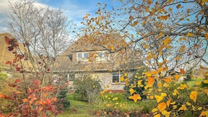 A house with a stone facade, surrounded by autumn foliage and a metal sculpture in the foreground. - Vacation apartment Eldorado Laacht (Norddorf)