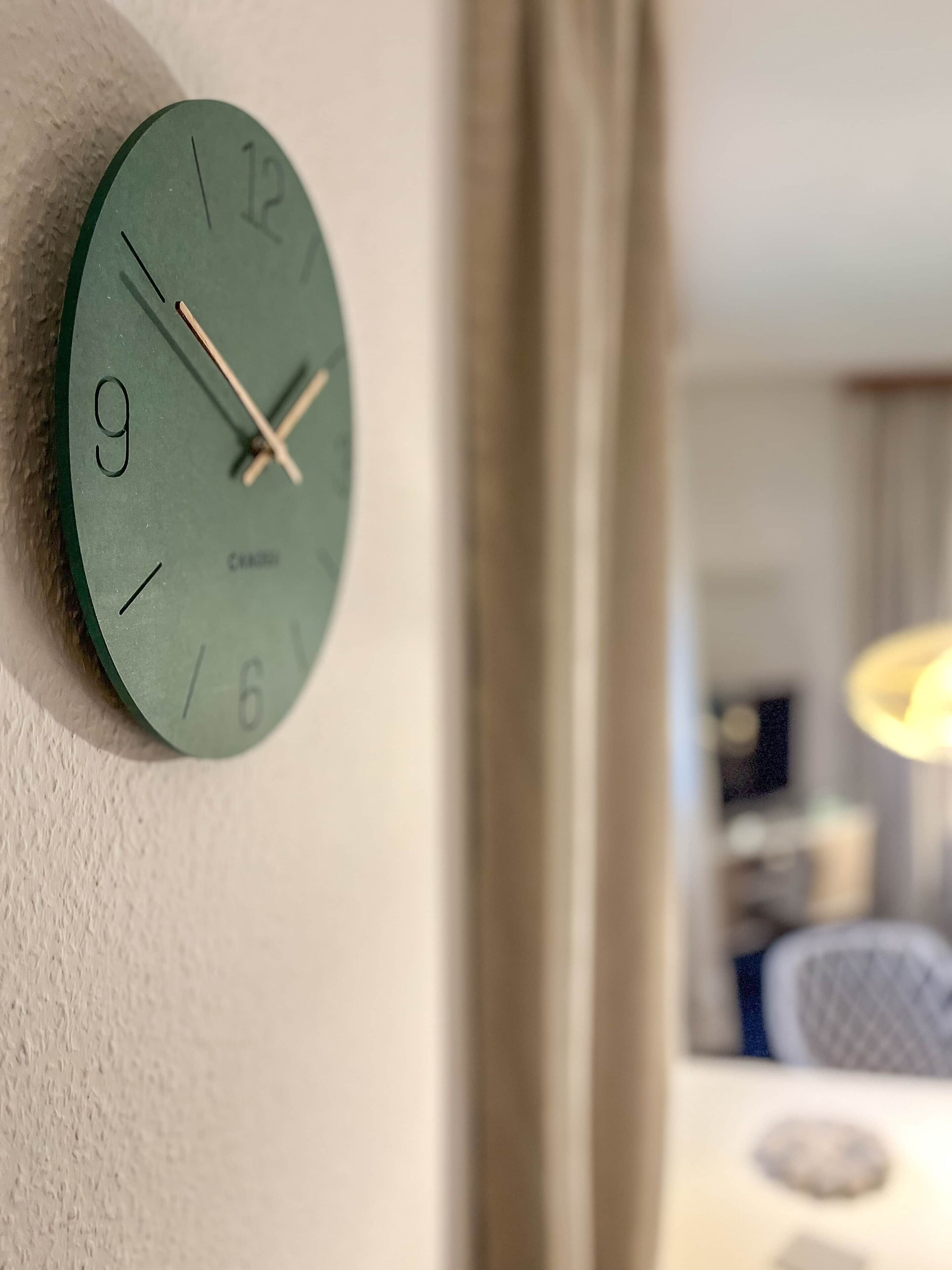 Een aan de muur bevestigd horloge met een groene wijzerplaat en Romeinse cijfers, wat een modern en minimalistisch ontwerp laat zien.