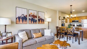 A living room with a gray sofa, wooden coffee table, and a dining area with wooden chairs and a kitchen in the background. - Walk to Gondola! Keystone Gem in River Run Village (Keystone)