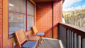 A balcony with two wooden chairs and a table, a brick wall, and a view of a snowy mountain. - Walk to Gondola! Keystone Gem in River Run Village (Keystone)