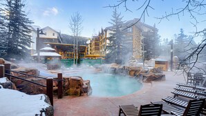 A spa area with a hot spring, wooden lounge chairs, and a building with multiple balconies. - Walk to Gondola! Keystone Gem in River Run Village (Keystone)