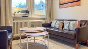 Ett vardagsrum med en brun lädersoffa, ett runt vitt bord och ett fönster med gardiner.