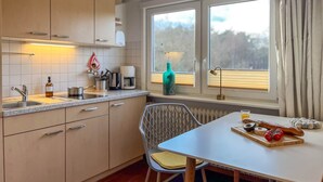 Ett modernt kök med en matplats, med ett fönster med gardiner, ett bord med mat på och en stol.